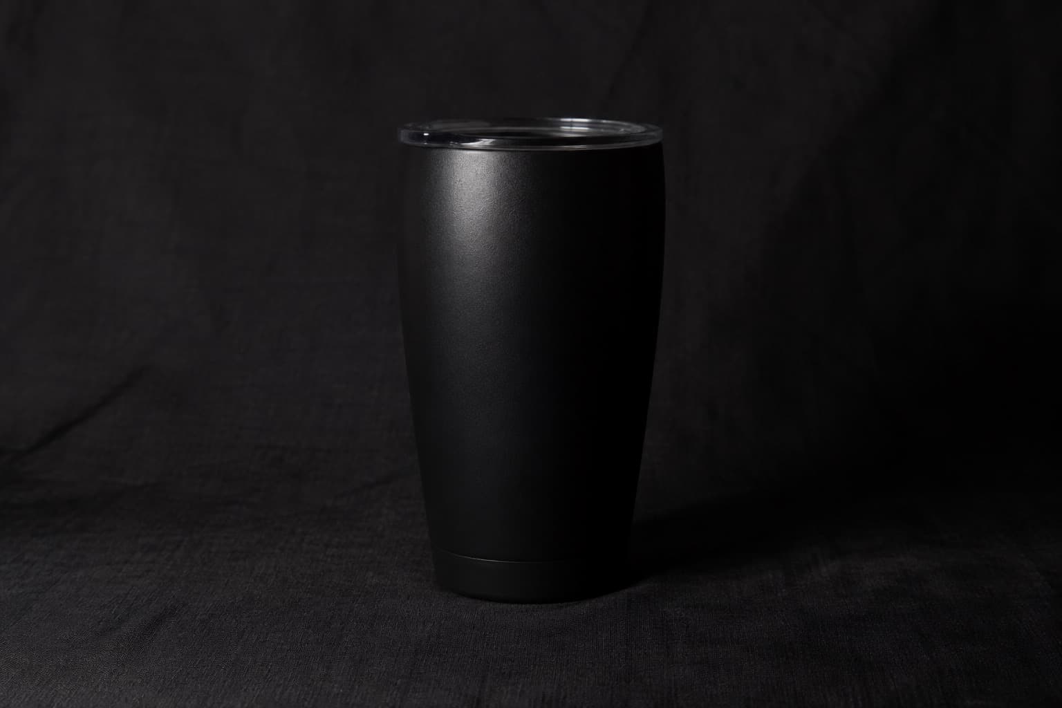 어두운 검정 천 배경과 겹쳐 오른쪽 윤곽과 표면 질감이 잘 보이지 않는 무광 검정 텀블러